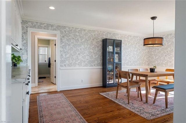 dining space with a wainscoted wall, wallpapered walls, crown molding, and wood finished floors