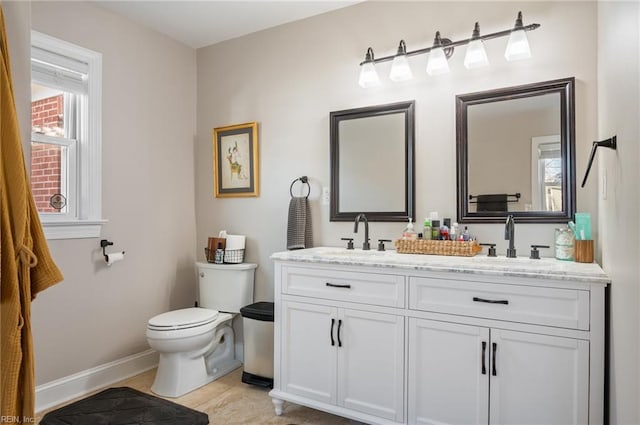 bathroom featuring double vanity, toilet, baseboards, and a sink