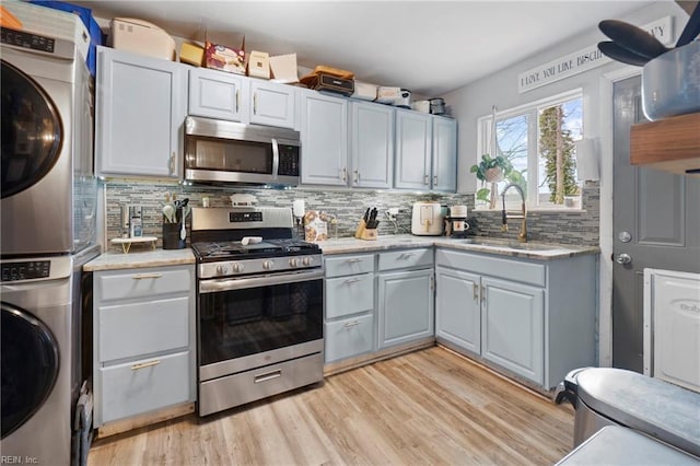 kitchen featuring tasteful backsplash, stacked washer / dryer, appliances with stainless steel finishes, and a sink