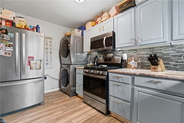 kitchen featuring gray cabinetry, decorative backsplash, stainless steel appliances, stacked washer and clothes dryer, and light wood-type flooring