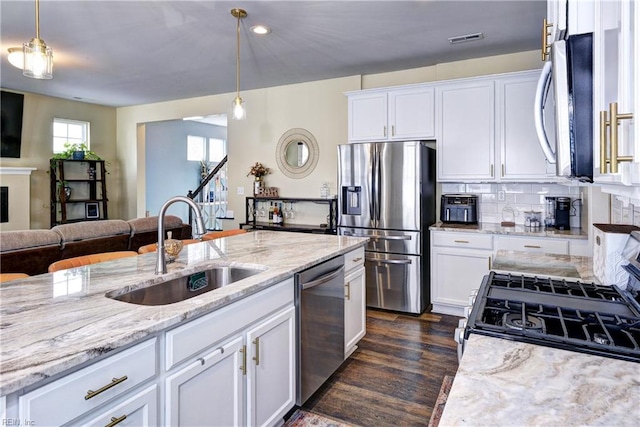 kitchen featuring visible vents, a sink, light stone counters, open floor plan, and appliances with stainless steel finishes