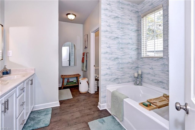 bathroom with vanity, wood finished floors, baseboards, wallpapered walls, and a garden tub