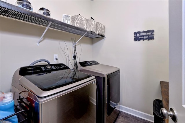 clothes washing area with laundry area, washing machine and dryer, dark wood-type flooring, and baseboards