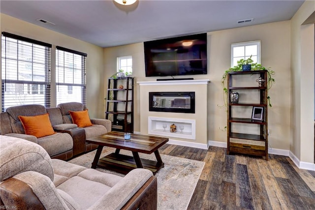 living room featuring visible vents, wood finished floors, baseboards, and a glass covered fireplace