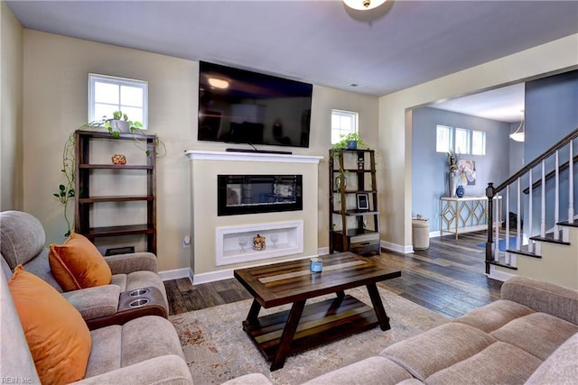 living area with baseboards, wood finished floors, a glass covered fireplace, and stairs