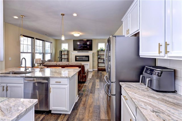 kitchen featuring open floor plan, a glass covered fireplace, white cabinets, stainless steel appliances, and a sink