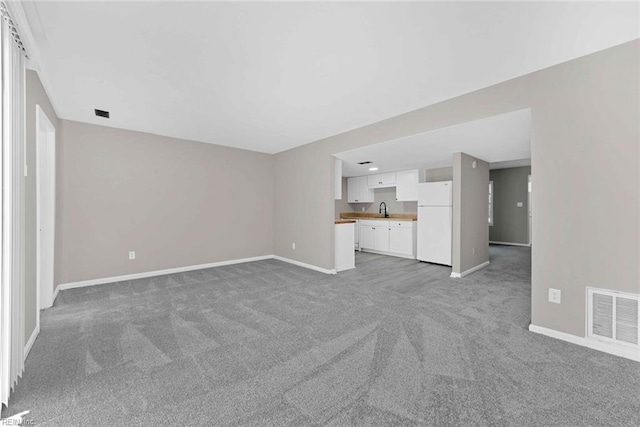 unfurnished living room featuring light carpet, visible vents, baseboards, and a sink