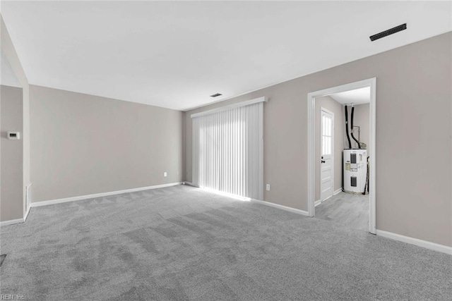 unfurnished room featuring visible vents, baseboards, electric water heater, and carpet