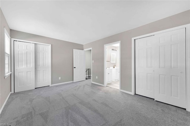 unfurnished bedroom with two closets, baseboards, ensuite bathroom, and carpet