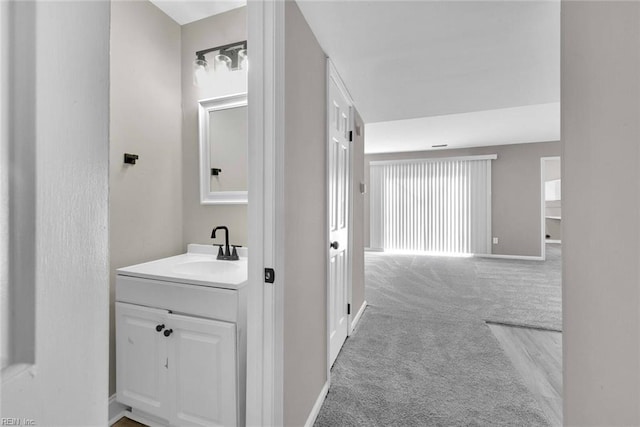 hallway featuring light carpet, baseboards, and a sink