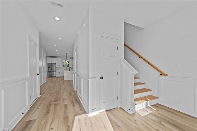 corridor featuring a decorative wall, visible vents, stairway, and light wood-style floors