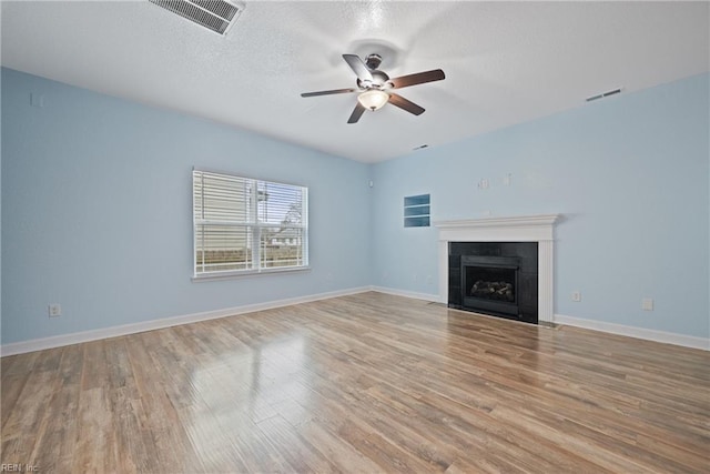 unfurnished living room featuring a fireplace, wood finished floors, visible vents, and ceiling fan