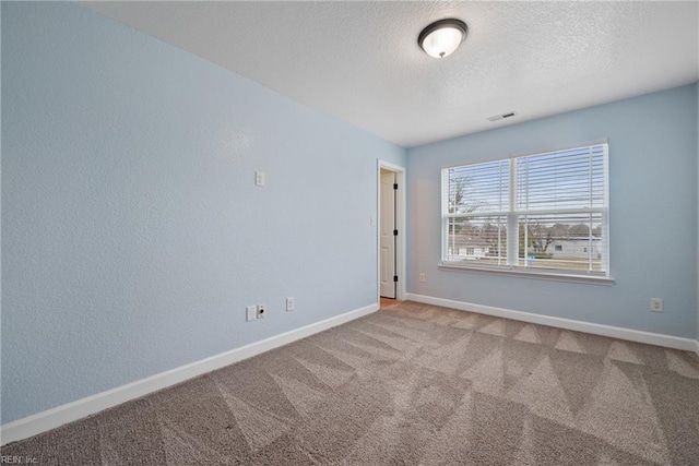 carpeted spare room with baseboards, visible vents, and a textured ceiling