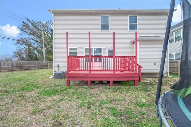 rear view of house with a fenced backyard, central AC unit, a yard, and a trampoline