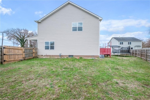 back of property with crawl space, a yard, a trampoline, and a fenced backyard