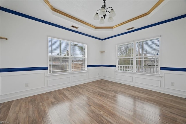 empty room with a raised ceiling, a notable chandelier, wood finished floors, and visible vents