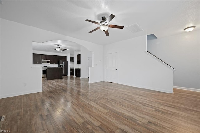 unfurnished living room with arched walkways, baseboards, ceiling fan, and wood finished floors