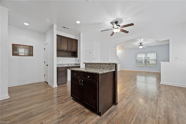 kitchen with visible vents, baseboards, light wood-style flooring, arched walkways, and dark brown cabinets