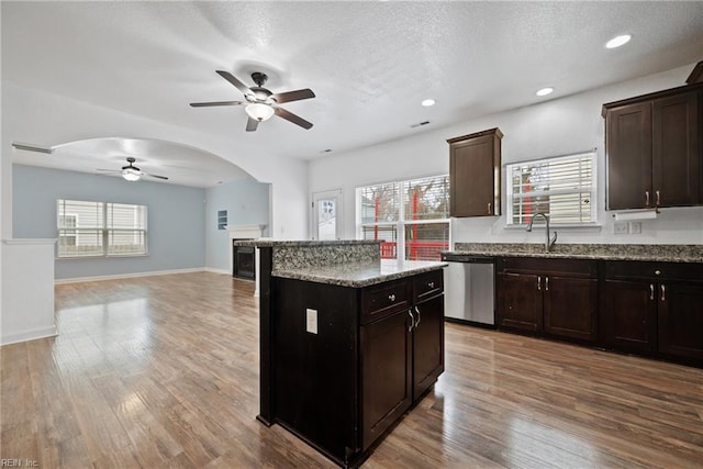 kitchen featuring stainless steel dishwasher, wood finished floors, arched walkways, and a kitchen island