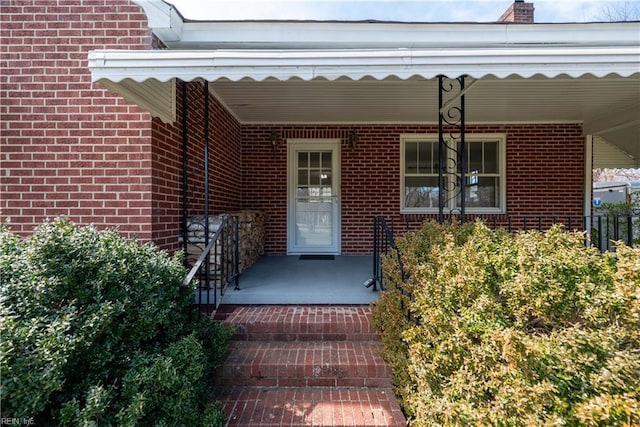 entrance to property featuring a porch and brick siding