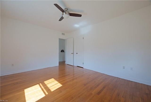 empty room featuring a ceiling fan, light wood-style flooring, visible vents, and baseboards