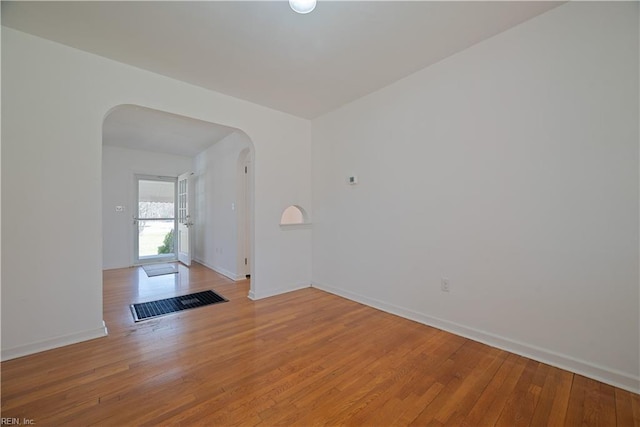 unfurnished room with baseboards, arched walkways, and light wood finished floors