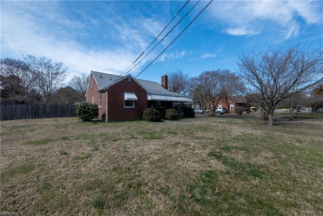 view of side of property with fence, a lawn, brick siding, and a chimney