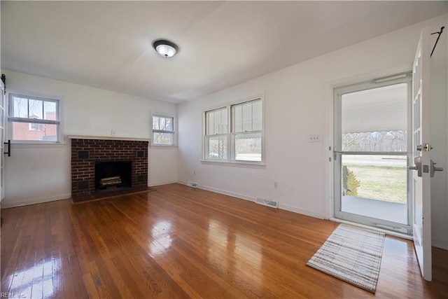 unfurnished living room with a fireplace, visible vents, wood-type flooring, and baseboards