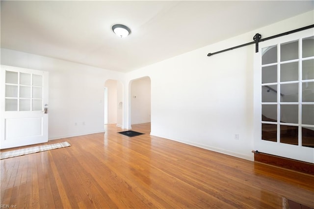 spare room with a barn door, arched walkways, and wood-type flooring