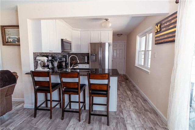 kitchen featuring backsplash, appliances with stainless steel finishes, a peninsula, white cabinetry, and a sink