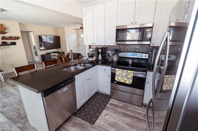 kitchen with decorative backsplash, appliances with stainless steel finishes, a peninsula, white cabinets, and a sink