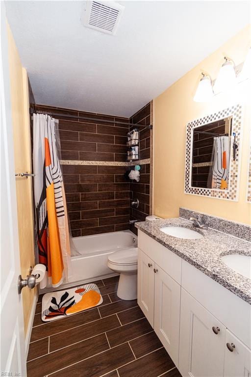 bathroom featuring visible vents, wood finish floors, double vanity, a sink, and toilet