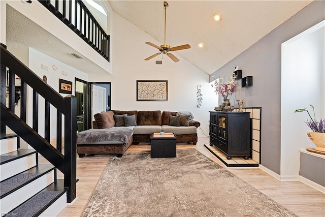 living area with stairway, a ceiling fan, wood finished floors, visible vents, and a towering ceiling