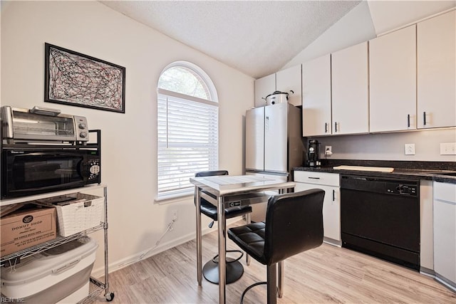 kitchen featuring light wood-type flooring, black dishwasher, dark countertops, freestanding refrigerator, and vaulted ceiling