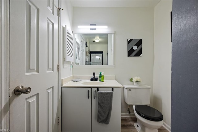 half bathroom with toilet, vanity, baseboards, and wood finished floors