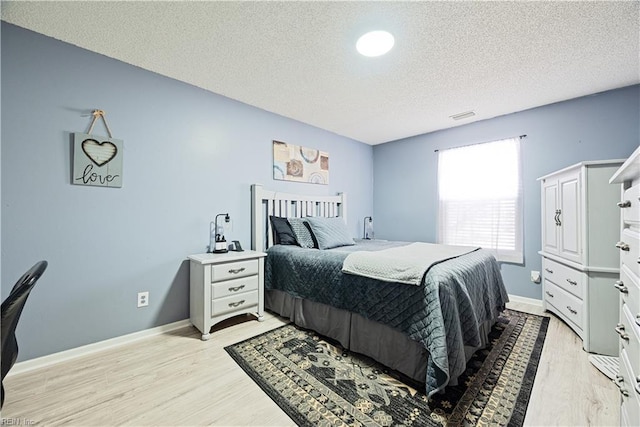 bedroom featuring baseboards, visible vents, light wood-type flooring, and a textured ceiling