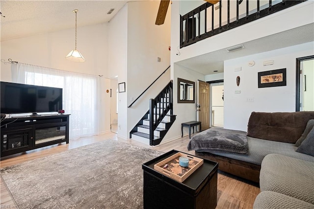 living area featuring visible vents, high vaulted ceiling, wood finished floors, and stairs