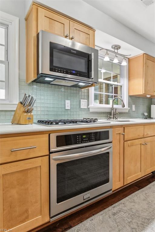 kitchen featuring backsplash, light brown cabinetry, light countertops, appliances with stainless steel finishes, and a sink