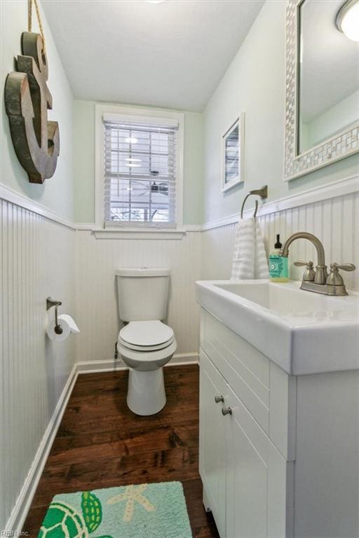 half bath with a wainscoted wall, toilet, wood finished floors, and vanity