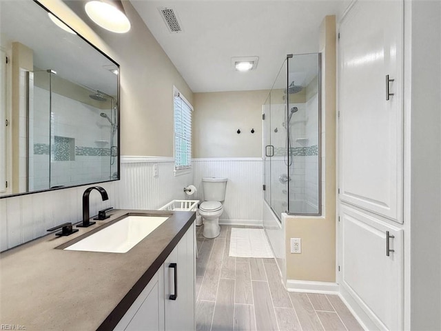 full bathroom featuring visible vents, wood finish floors, toilet, wainscoting, and vanity