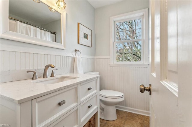 full bath featuring vanity, tile patterned floors, toilet, and wainscoting