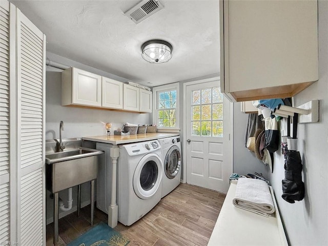 washroom featuring visible vents, washing machine and clothes dryer, cabinet space, a sink, and light wood-style floors