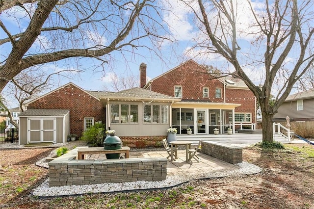 back of property with an outbuilding, a shed, a sunroom, a chimney, and a patio area