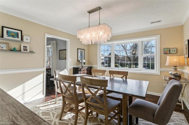 dining room featuring visible vents, wood finished floors, baseboards, and ornamental molding