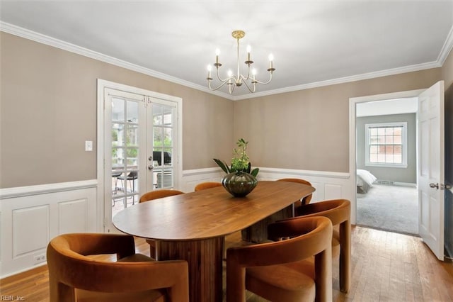 dining area with a wainscoted wall, ornamental molding, french doors, wood finished floors, and a notable chandelier