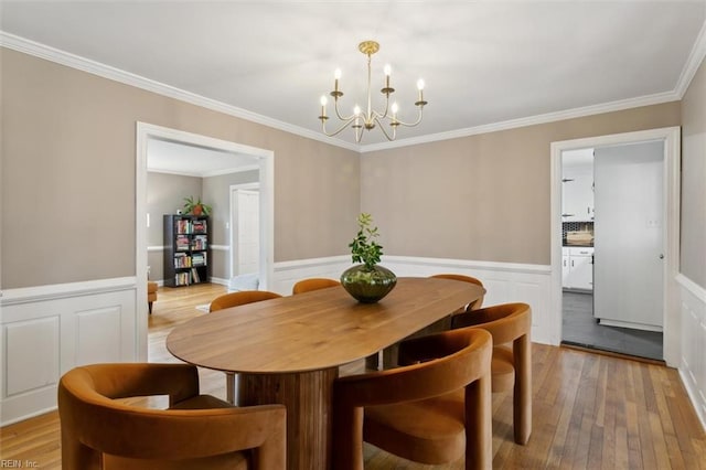 dining area featuring an inviting chandelier, light wood-style flooring, crown molding, and a wainscoted wall