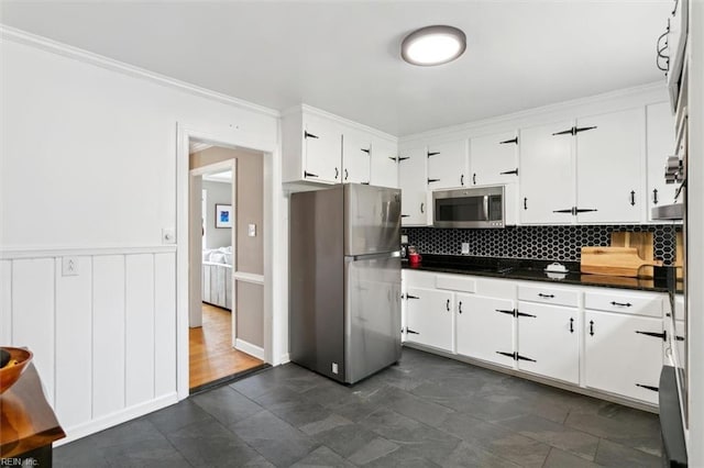 kitchen with decorative backsplash, crown molding, appliances with stainless steel finishes, white cabinetry, and dark countertops