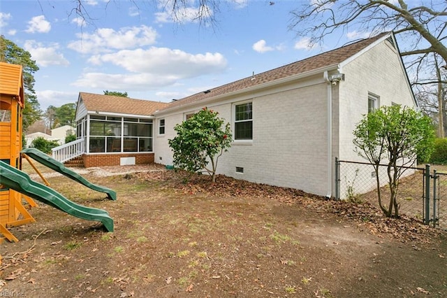 rear view of house featuring fence, a playground, a sunroom, crawl space, and brick siding