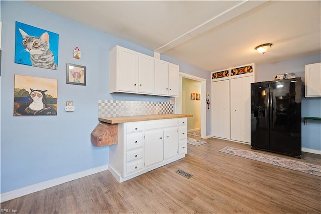 kitchen with black fridge with ice dispenser, backsplash, white cabinetry, and light wood-type flooring