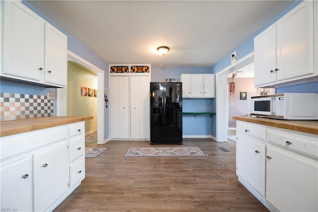 kitchen with white microwave, wooden counters, light wood-style flooring, white cabinets, and black refrigerator with ice dispenser